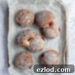 Vegan jam doughnuts on a parchment lined baking sheet.
