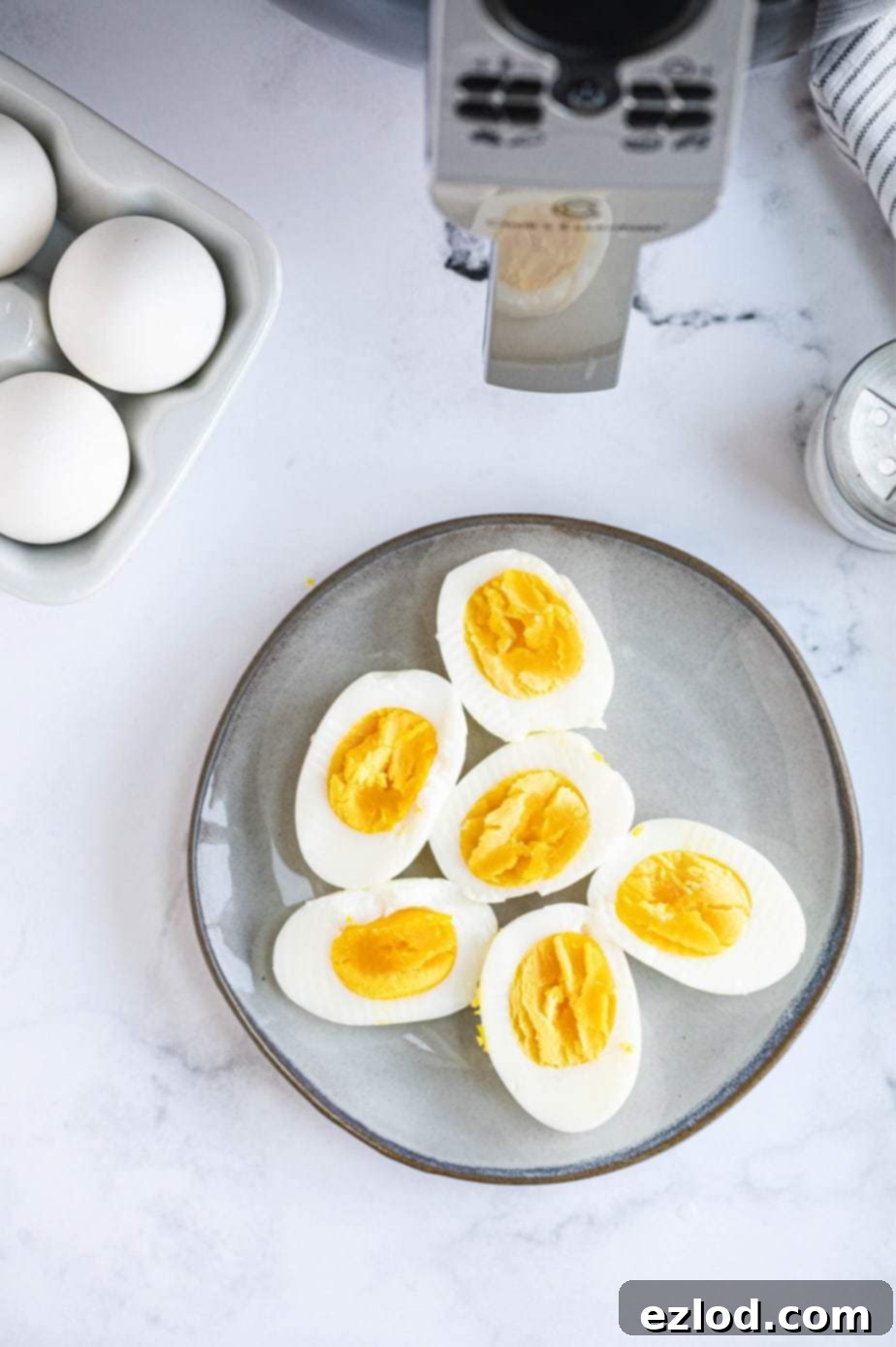 A plate of hard boiled eggs is placed next to raw eggs and an air fryer, illustrating the journey from raw to cooked.