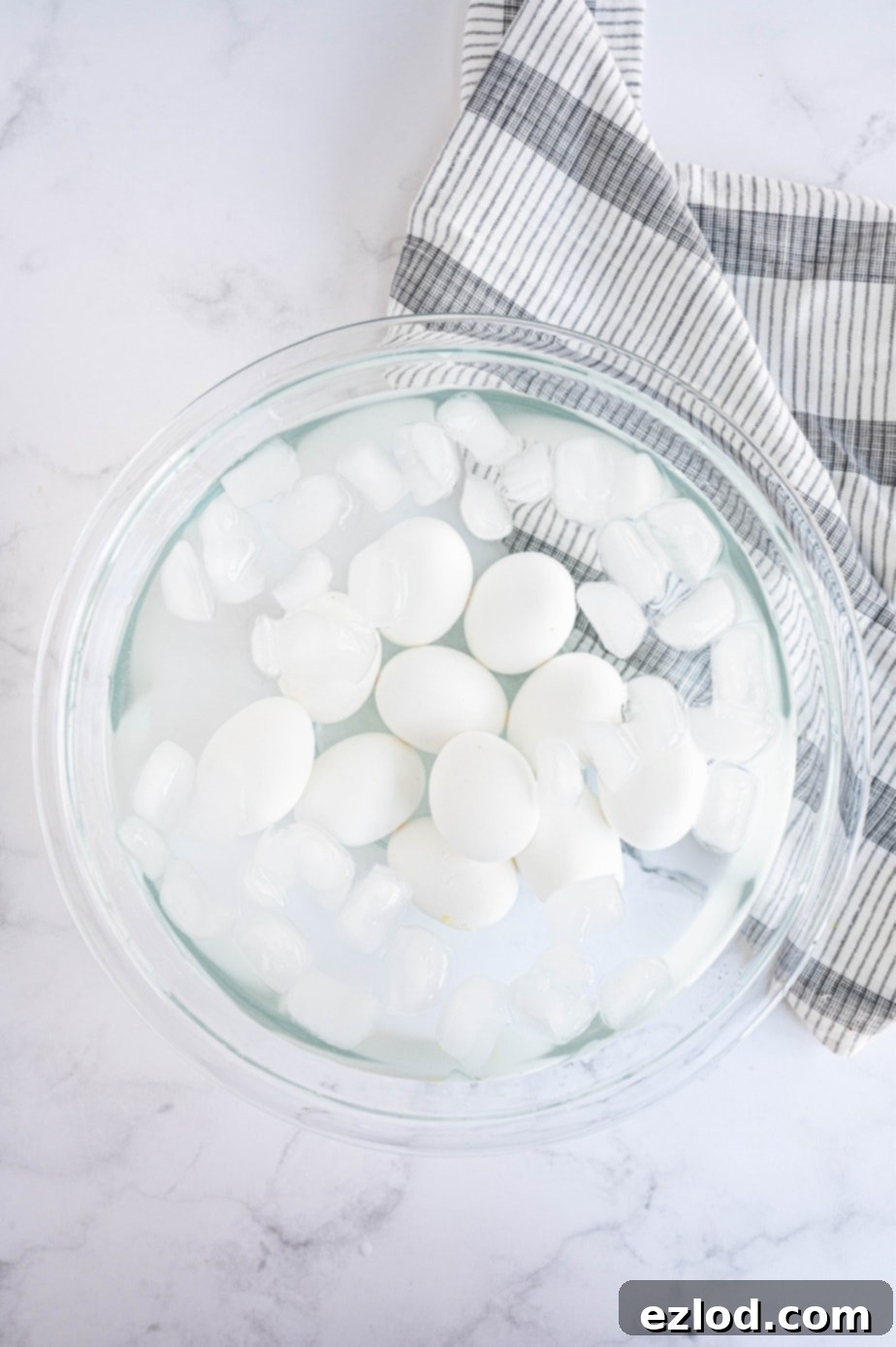 Cooked eggs are in a large glass bowl filled with ice and water, illustrating the essential ice bath step.