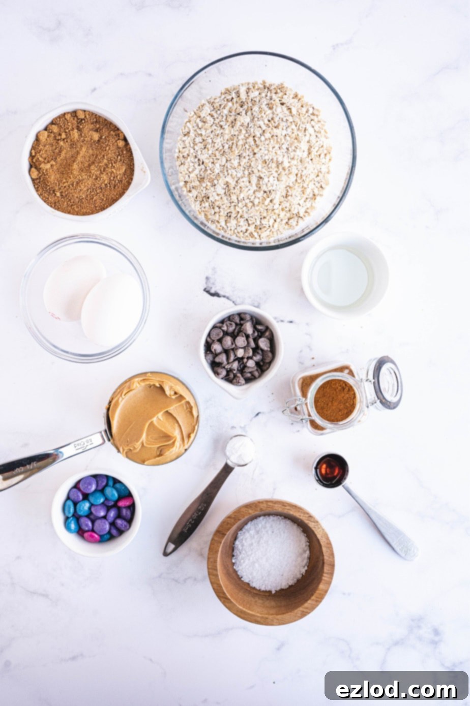 All the dry ingredients for monster cookies are artfully arranged on a white surface, showcasing the wholesome components before mixing.