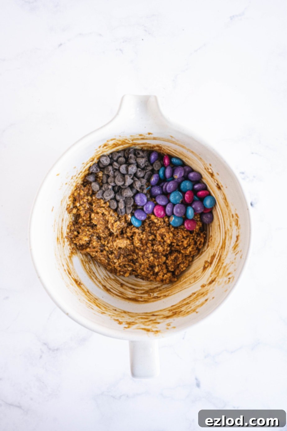 The mixing bowl now holds the combined wet and dry ingredients for monster cookies, forming a thick, ready-to-scoop dough.