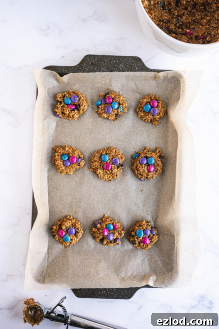 Nine perfectly formed monster cookie dough balls, ready for the oven, are arranged on a parchment-lined baking sheet.