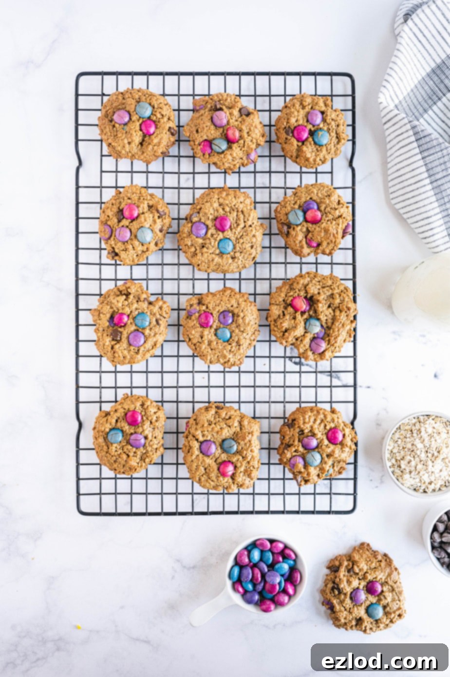 A dozen freshly baked monster cookies are cooling on a wire rack, their vibrant candies and rich texture visible.