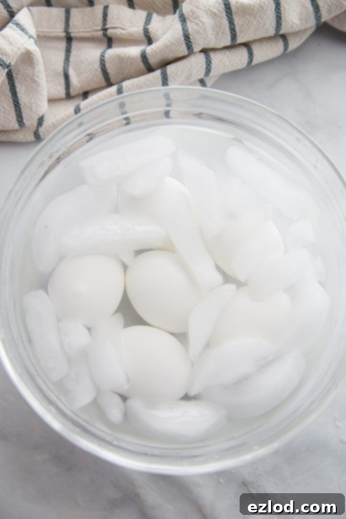 Freshly cooked eggs cooling in an ice bath within a clear glass bowl on a kitchen counter.
