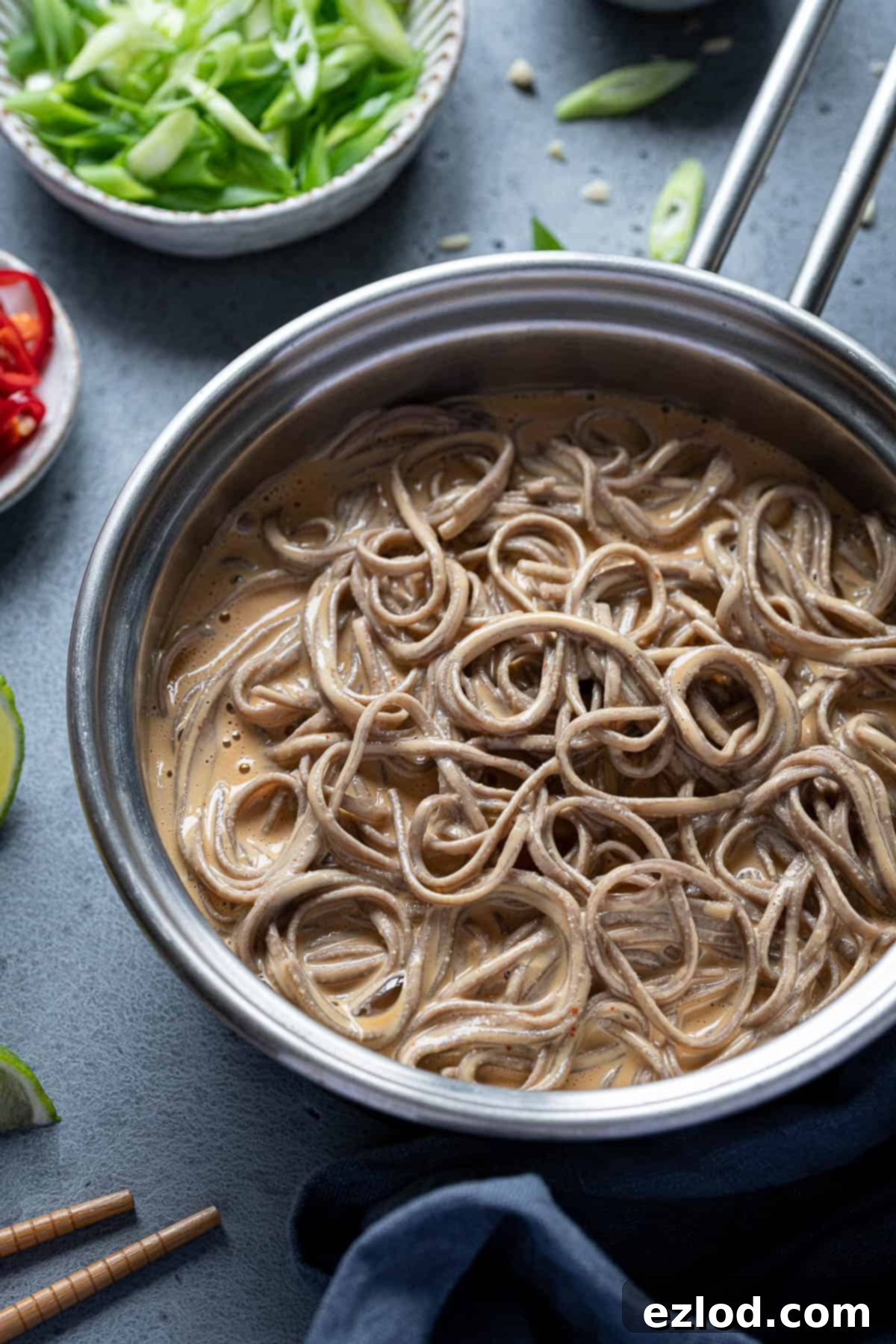 Deliciously coated creamy peanut noodles in a pan. Close-up view of creamy peanut noodles being tossed in a pan, showcasing their rich, glossy texture and the delightful coating of the sauce.