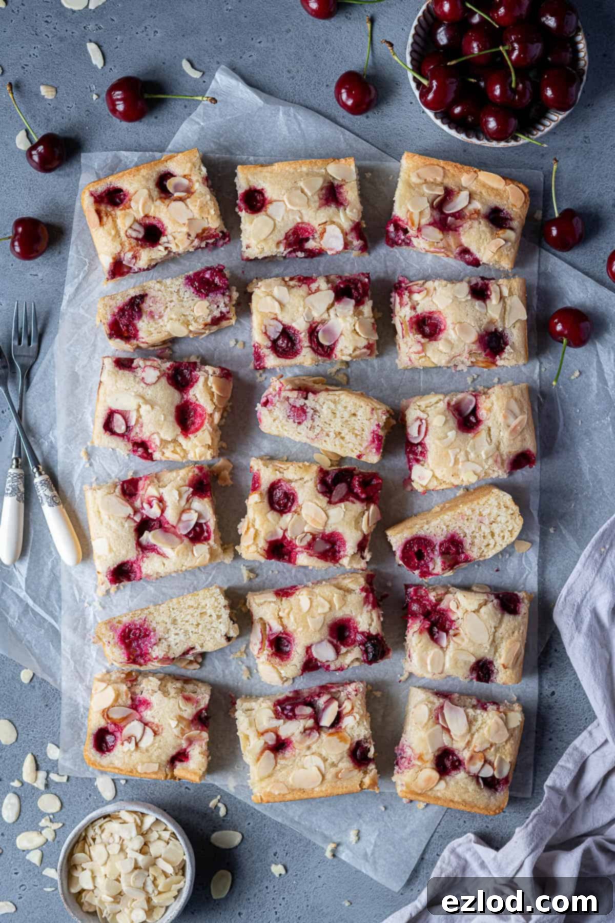 Freshly baked vegan cherry almond cake, cut into perfect squares and arranged on a sheet of baking parchment, ready for serving.