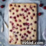 Vegan cherry almond cake on a sheet of baking parchment with bowls of cherries and flaked almonds.