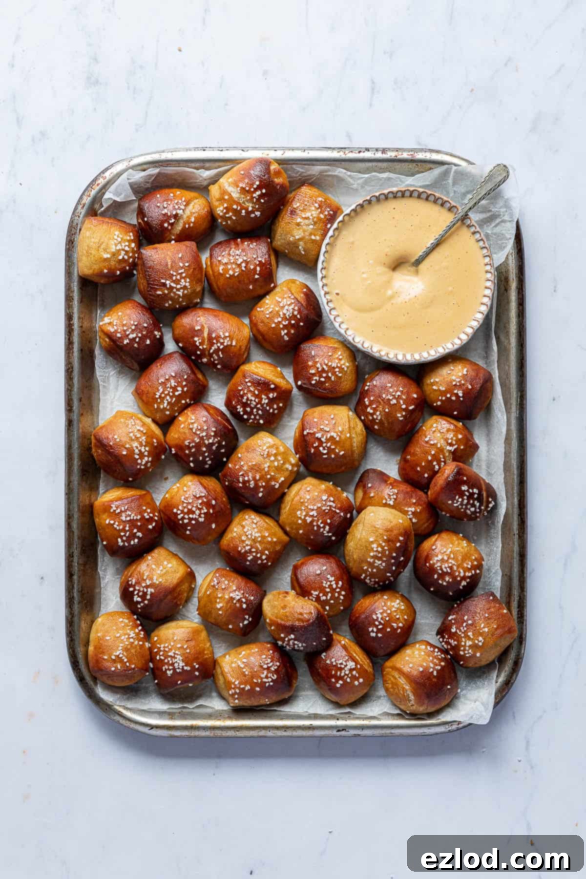 A tray of vegan pretzel bites with a bowl of dipping sauce on a marble background.