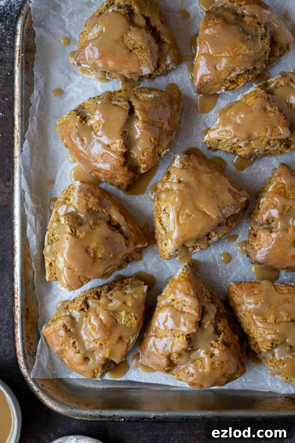A fresh batch of glazed vegan pumpkin scones arranged on a metal baking tray, ready to be enjoyed.