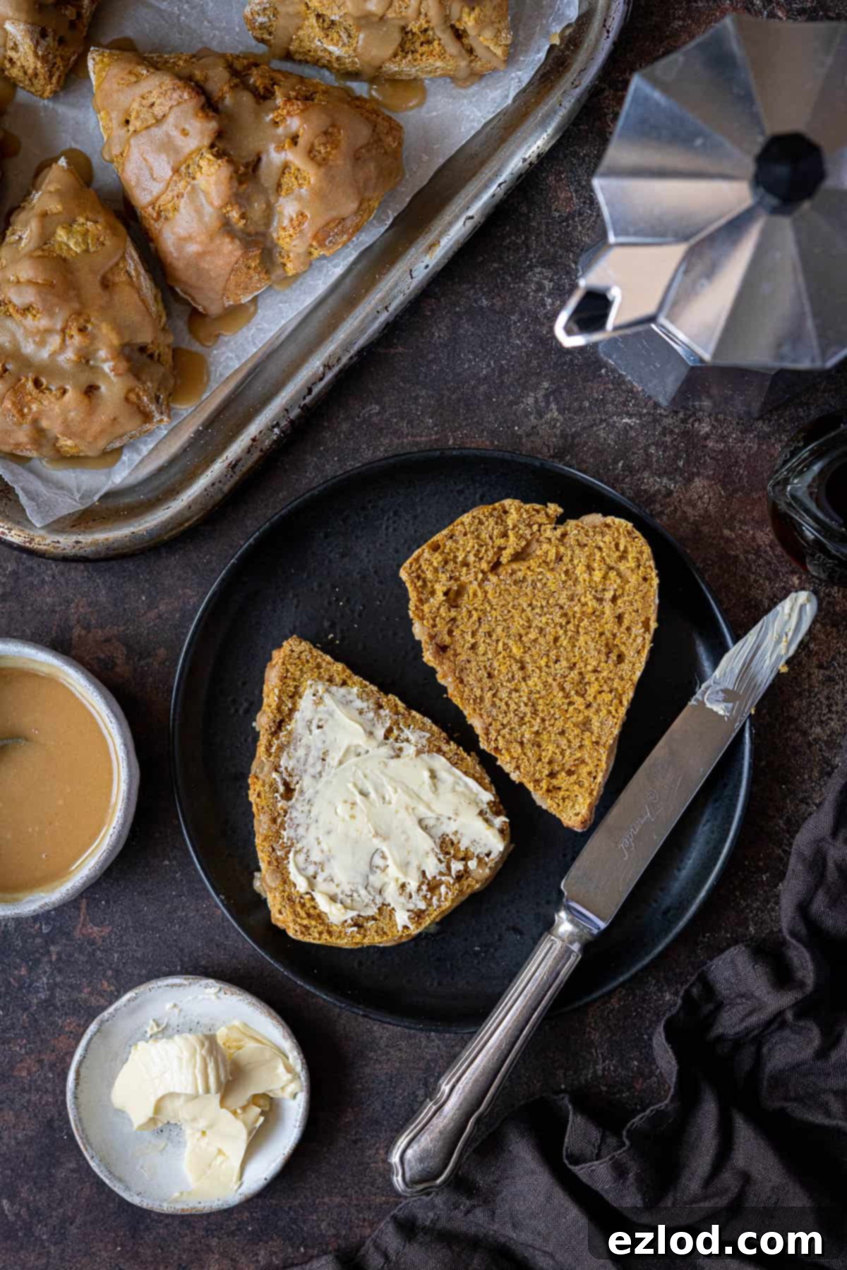 A freshly baked vegan pumpkin scone sliced in half and spread with butter, presented on a minimalist black plate.