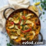 A pan of vegan vegetable paella on a wooden board on a blue background with a beige cloth, glass of water and fresh parsley.