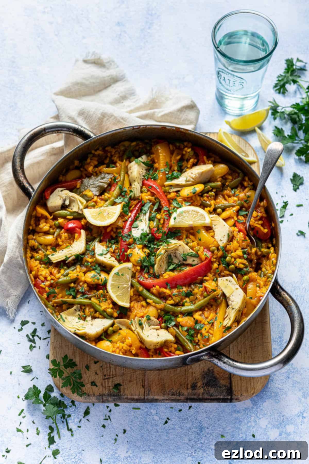 Apan of vegan vegetable paella on a wooden board on a blue background.