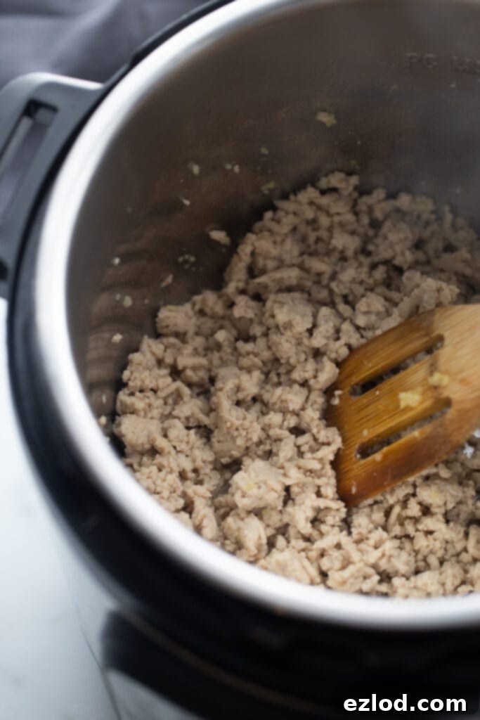 Overhead photo of cooked ground chicken in the Instant Pot with a wooden slotted spoon.