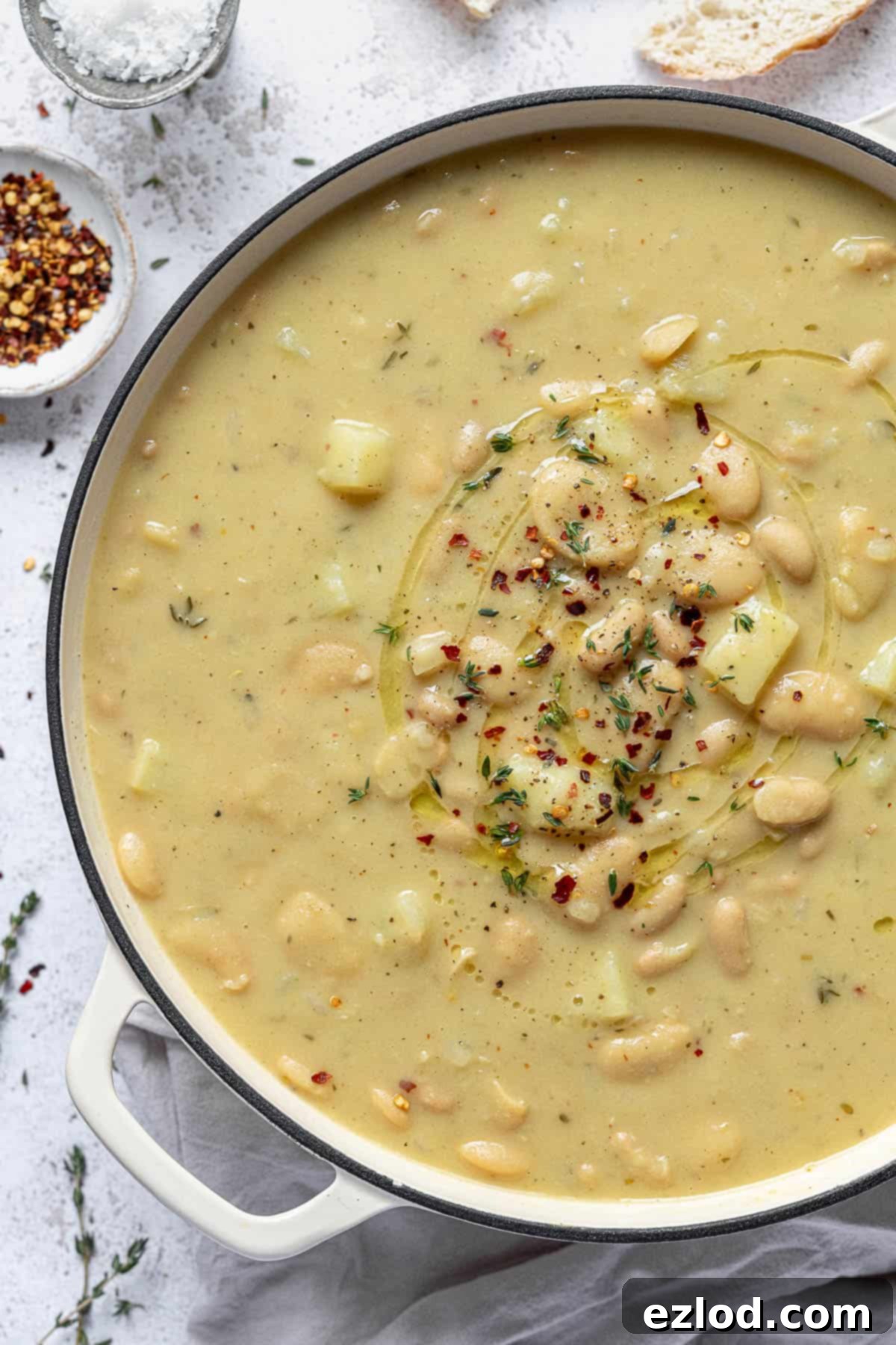 A close-up view of creamy white bean soup simmering gently in a large, pristine white pot on a stovetop, highlighting its rich texture and inviting warmth before blending.