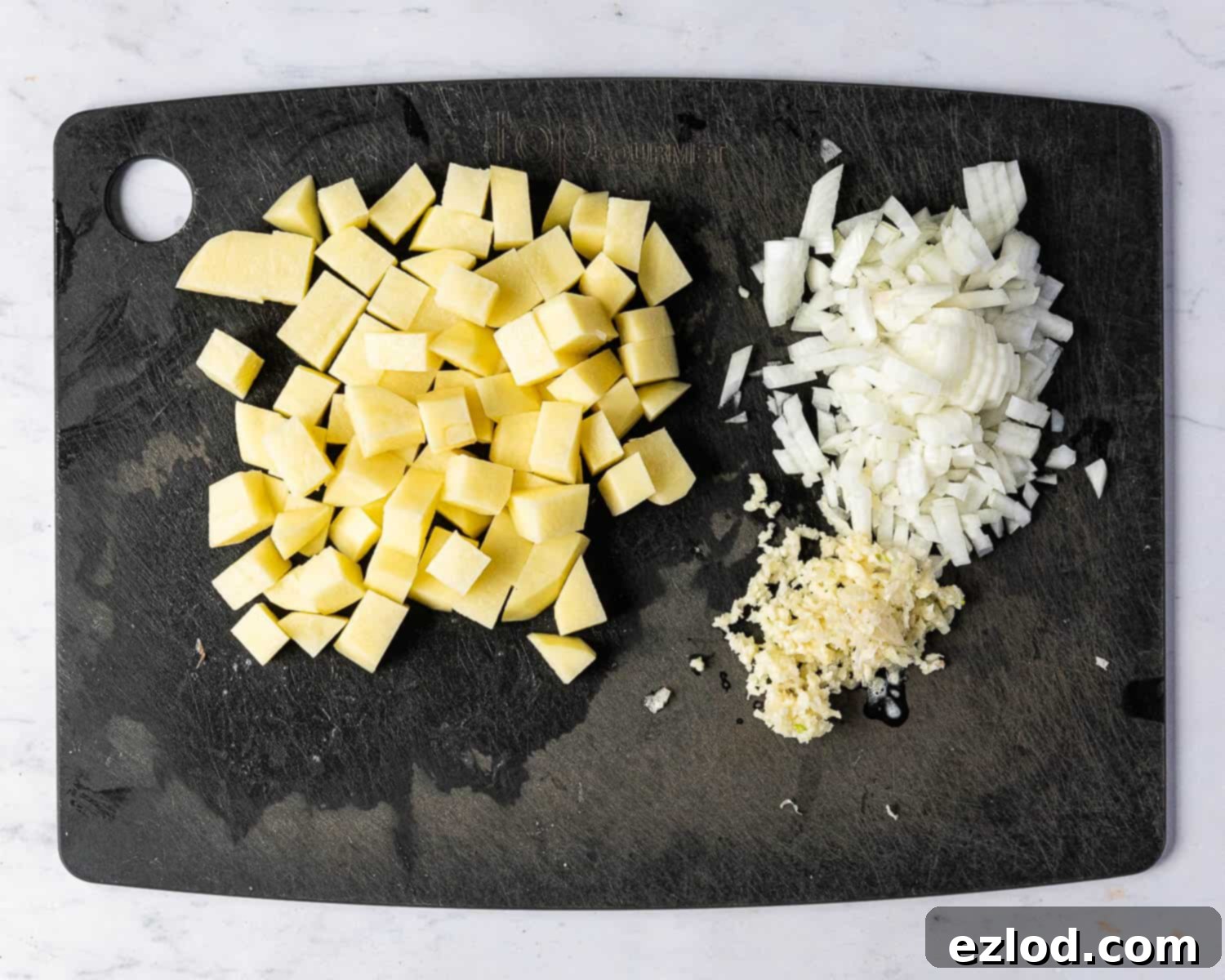 Step one: Finely chopped onion, uniformly cubed potato, and crushed garlic cloves neatly arranged on a chopping board, indicating readiness for the cooking process.