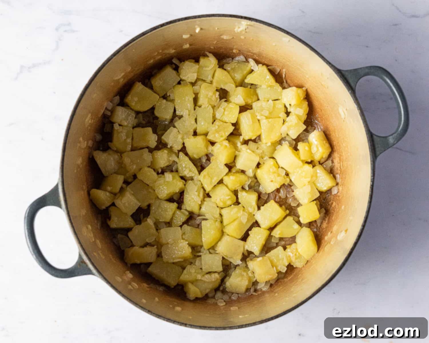 Step two: Onion, potato, and garlic gently sautéing in shimmering olive oil within a large saucepan over low heat, being frequently stirred to soften and develop aromatic flavors.