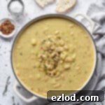 A white pan full of creamy white bean soup, served with crusty bread, salt, chilli flakes, and fresh thyme sprigs, on a clean white background.