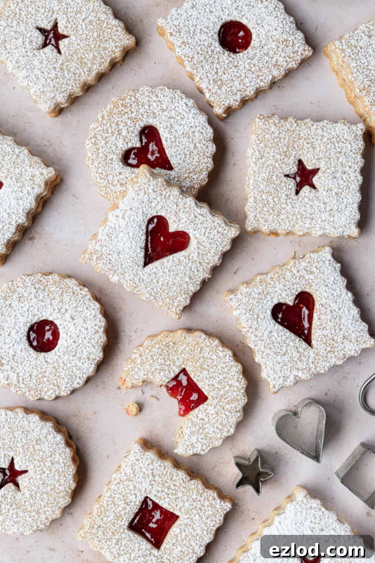 A close-up of delicious vegan Linzer cookies on a marble background, one with a bite taken out of it, showcasing the vibrant jam filling and delicate texture.