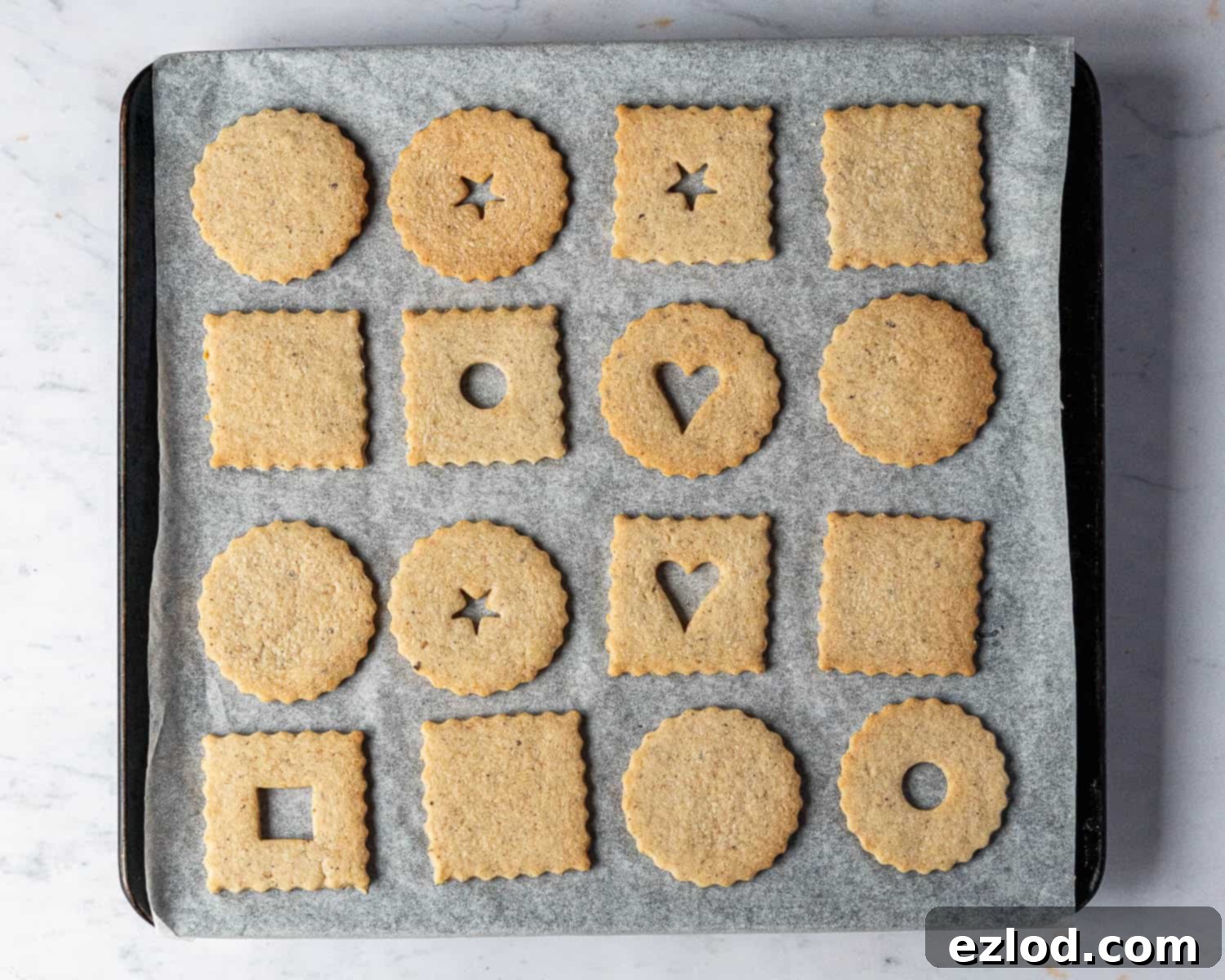Freshly baked Linzer cookie halves cooling on a baking sheet, showing their light golden edges.