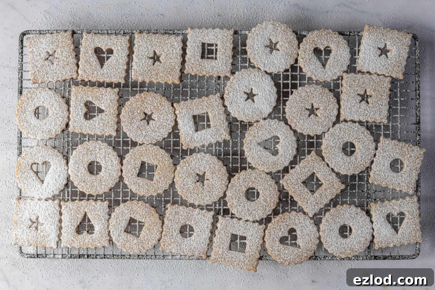 Several top halves of Linzer cookies, beautifully dusted with icing sugar, on a wire cooling rack.