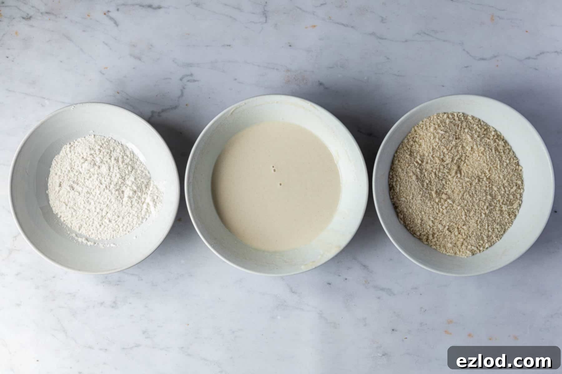 Step 8: Three shallow bowls are set up for the breadcrumb coating process: one with plain flour, one with a smooth non-dairy milk batter, and one with crisp panko breadcrumbs. This shows the organized station for coating the vegan 'fish' cakes to achieve a perfectly crispy finish.