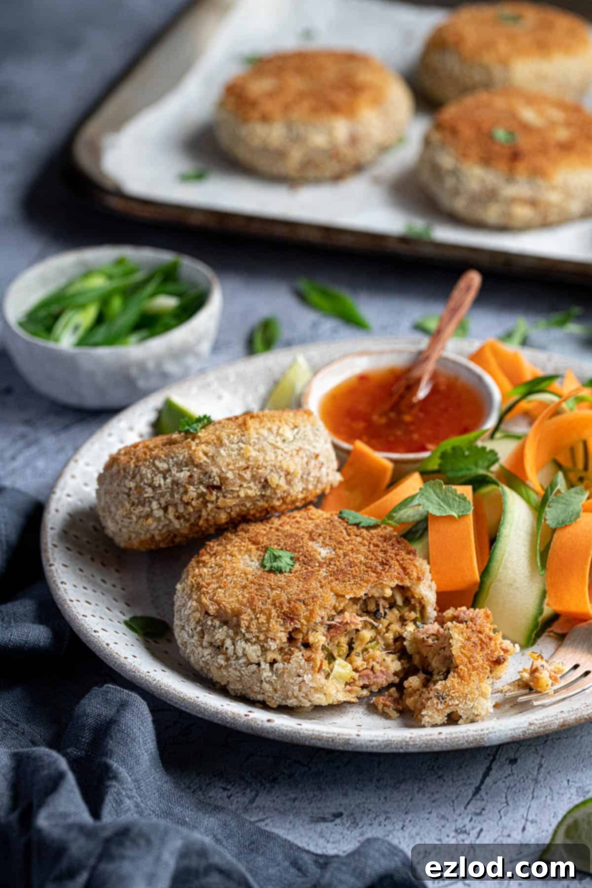 A close-up shot of a vegan Thai red curry 'fish' cake on a plate, with a forkful gently removed to reveal its flaky, flavorful interior texture. The golden-brown exterior suggests a crispy finish, while the visible flecks of jackfruit or banana blossom highlight its plant-based authenticity.