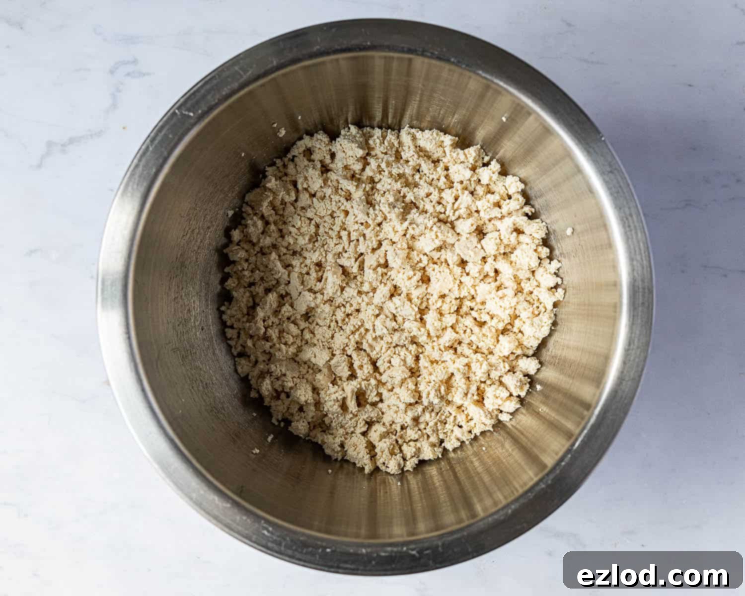 Step 3: Crumbled extra-firm tofu resting in a large mixing bowl, showing its readiness to be combined with other ingredients. The tofu has been pressed to remove excess liquid and broken into small, irregular pieces by hand, highlighting its role in the vegan 'fish' cakes.