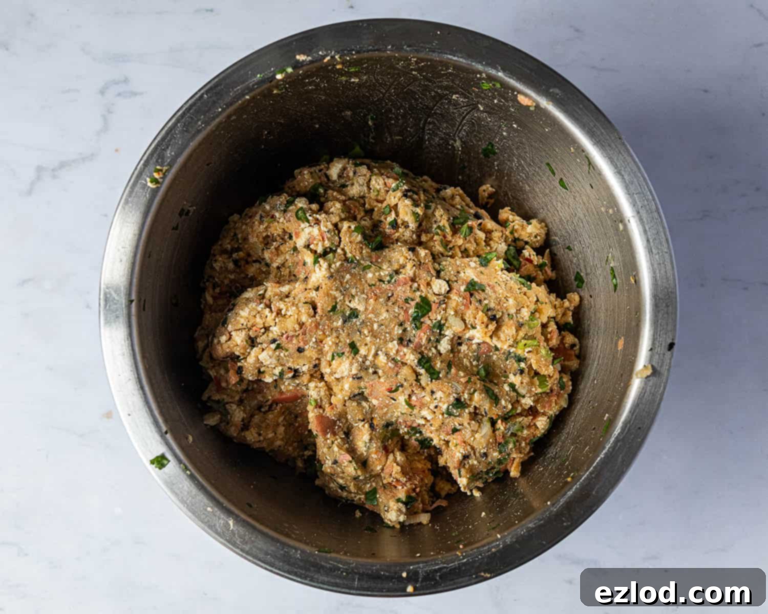 Step 6: A large mixing bowl filled with the complete vegan 'fish' cake mixture, showcasing all ingredients thoroughly combined. The texture appears uniform and ready for shaping, with visible flecks of herbs and the reddish hue from the Thai red curry paste.