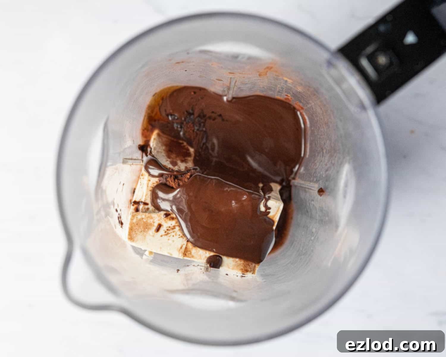 Step 2: All ingredients for the vegan chocolate orange pots – melted chocolate, silken tofu, cocoa, maple syrup, and orange extract – are gathered in a blender, ready for blending.