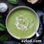 Creamy Vegan Broccoli Cheese Soup 10 A bowl of cheesy vegan broccoli soup on a wooden table with slices of bread, a bowl of salt, a grey cloth and fresh spinach leaves.