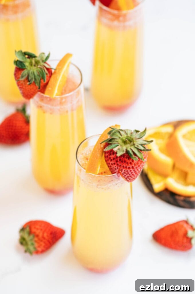 Champagne flutes with orange strawberry mimosas on a white table, adorned with strawberry garnishes, ready for a festive occasion
