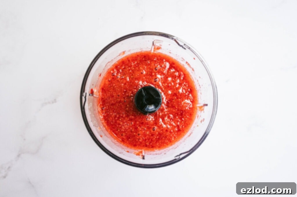 A small food processor filled with vibrant red strawberry puree, ready to be added to mimosas