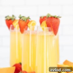 Orange Strawberry Mimosas in champagne flutes, garnished with fresh strawberries