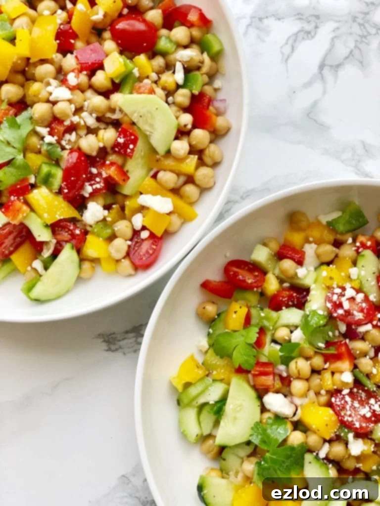 An overhead view of two bowls of vibrant Mediterranean Chickpea Salad, beautifully topped with crumbled feta cheese, presented on a white marble background, perfect for a healthy brunch.