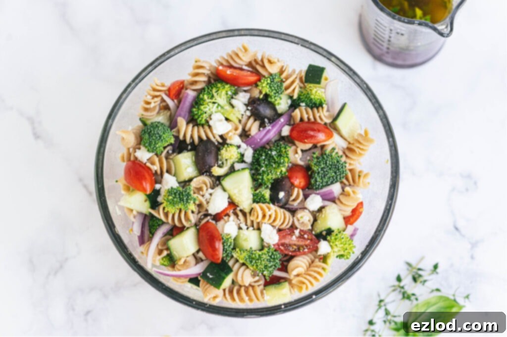 An elegant glass serving bowl brimming with a colorful Greek pasta salad, showcasing fresh vegetables and pasta, ready to be served at a brunch gathering.
