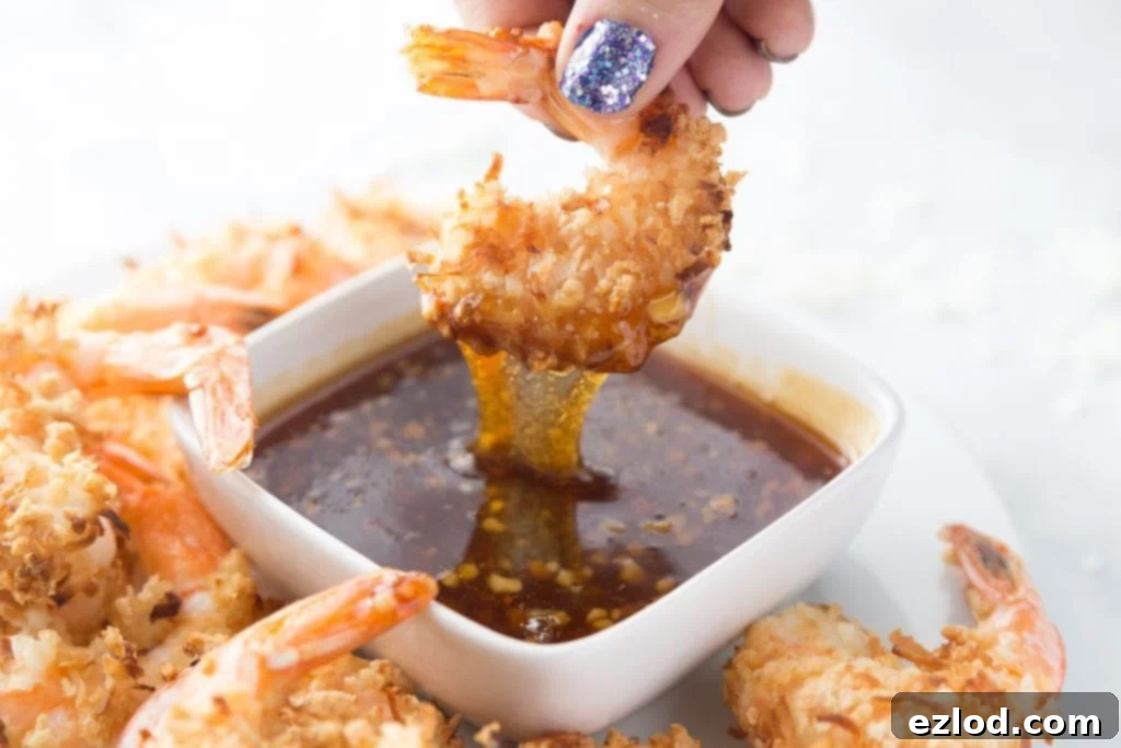 A close-up shot of a perfectly cooked coconut shrimp being dipped into a luscious homemade sweet chili sauce, highlighting its crispy texture and vibrant flavors, ideal for a healthy brunch appetizer.