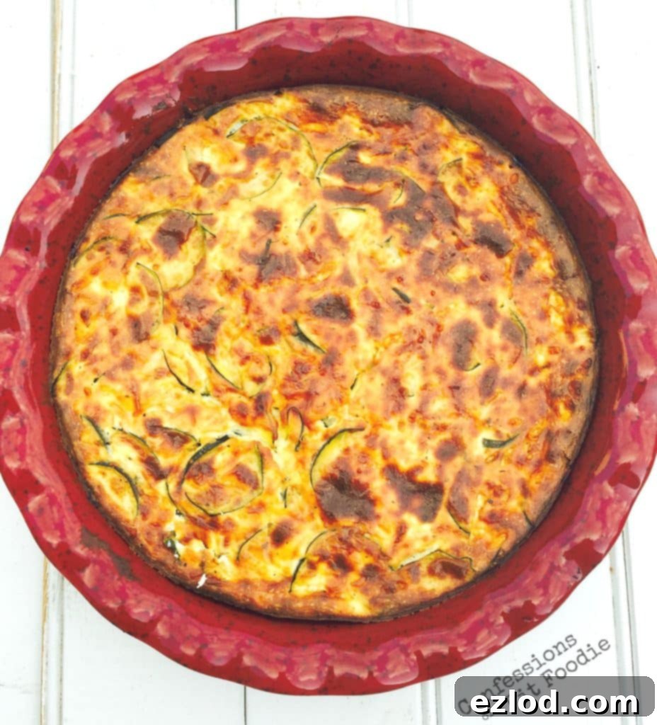 Crustless zucchini quiche, golden brown and perfectly baked, in a round ceramic pie plate on a rustic white wooden background, ready for a healthy brunch.
