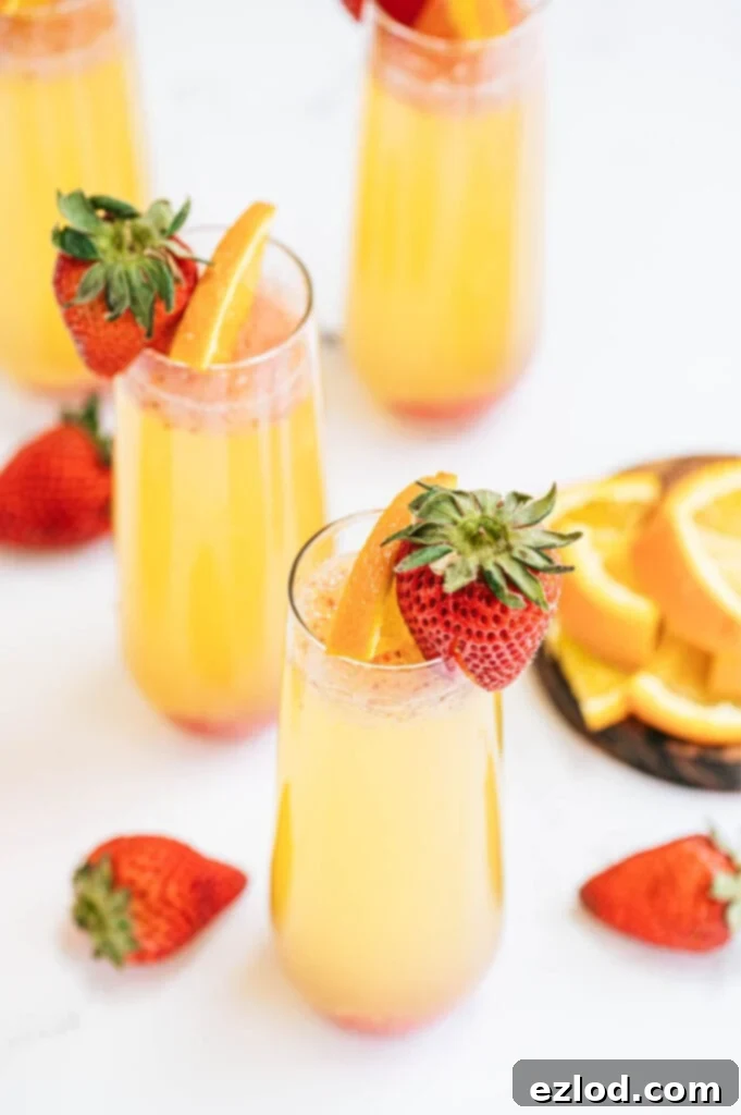 A beautifully presented Orange Strawberry Mimosa in a champagne flute, garnished with fresh fruit, set against a bright background, perfect for a festive brunch.