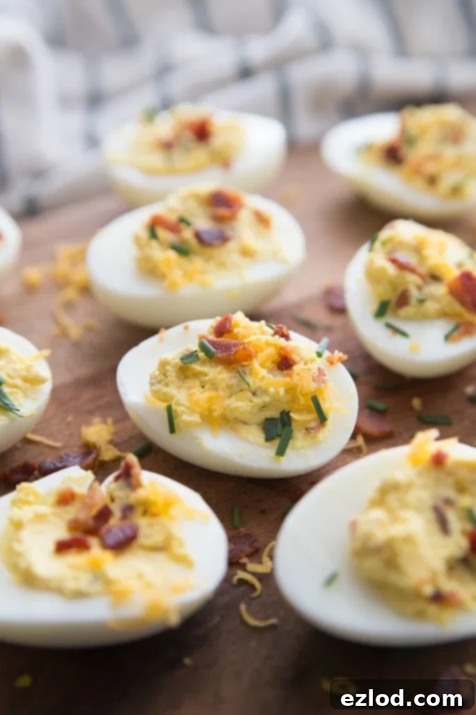 Many loaded deviled eggs, artfully arranged on a wooden surface, generously topped with crispy bacon bits and fresh chives, perfect as a healthy and flavorful brunch appetizer.