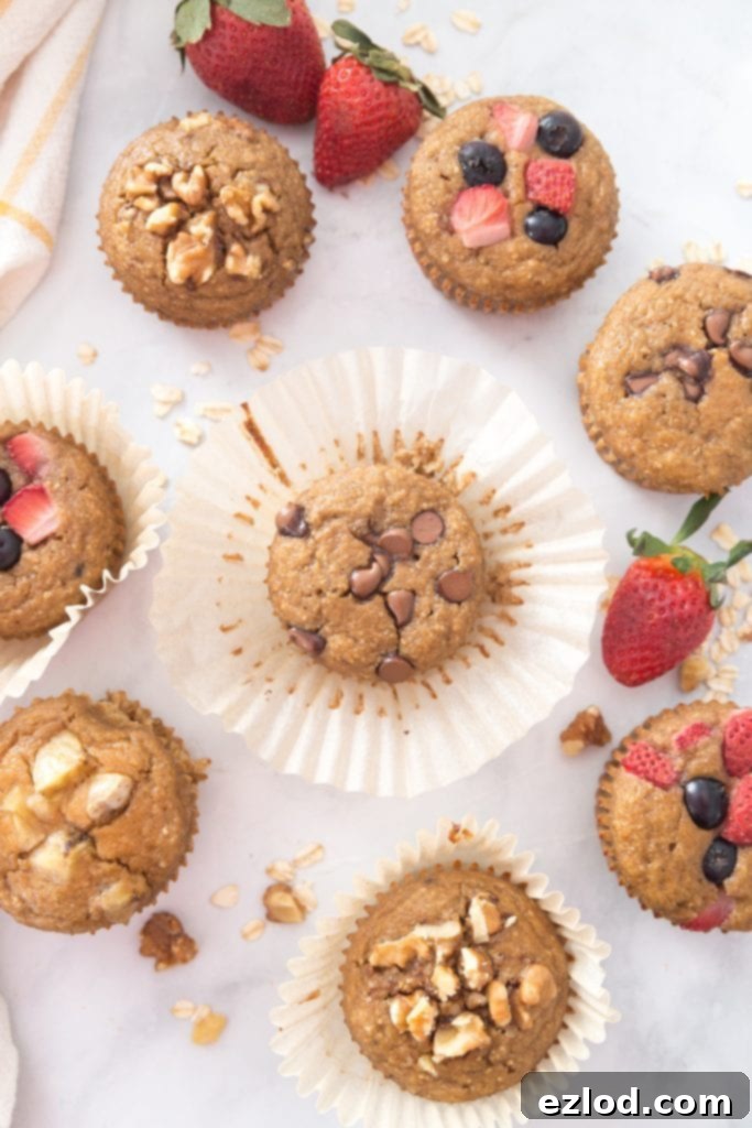 A delightful array of healthy banana oatmeal blender muffins with various toppings like nuts and fruit, beautifully arranged among fresh strawberries, oats, and walnuts.