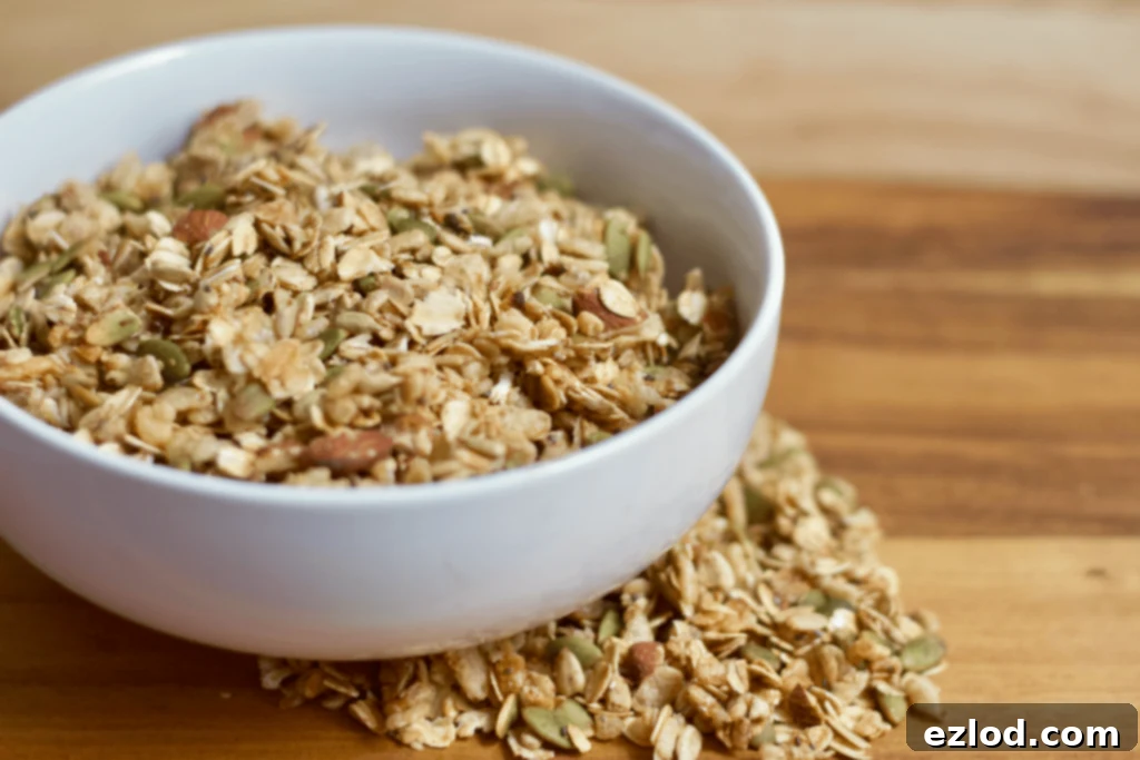 A bowl brimming with homemade healthy granola, with some scattered artfully on the side, all set against a warm wooden background, perfect for a DIY brunch parfait bar.