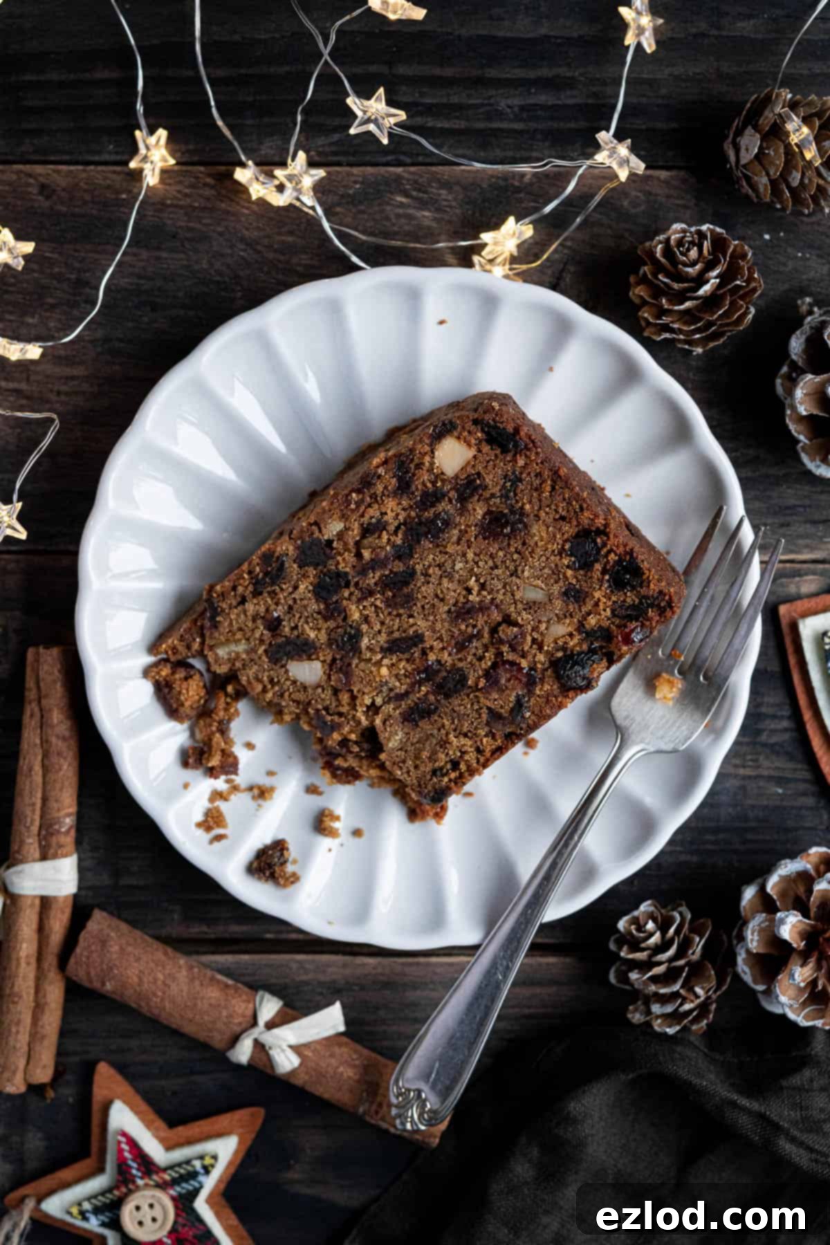 A slice of gluten-free vegan Christmas cake on a white plate with a forkful removed, showcasing its rich texture.