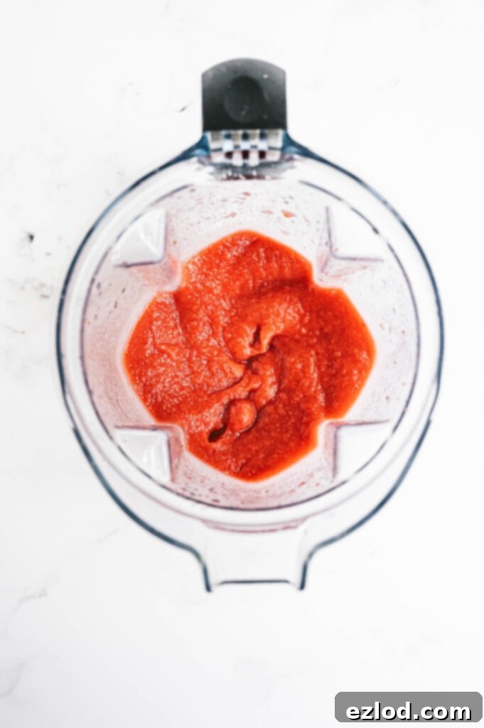 An overhead shot of the perfectly blended, smooth, and vibrant pink Frozen Strawberry Rhubarb Margarita mixture inside the blender, showcasing its luscious, slushy consistency, ready to be served.
