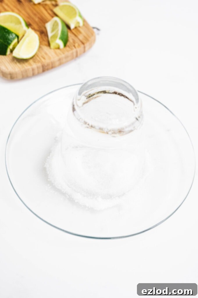 A close-up shot of a cocktail glass with its rim perfectly coated in coarse white salt, sitting on a small white plate, ready to be filled with a refreshing margarita.