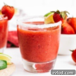 A vibrant Frozen Strawberry Rhubarb Margarita in a salt-rimmed glass, garnished with lime and strawberry, showcasing the refreshing summer cocktail.