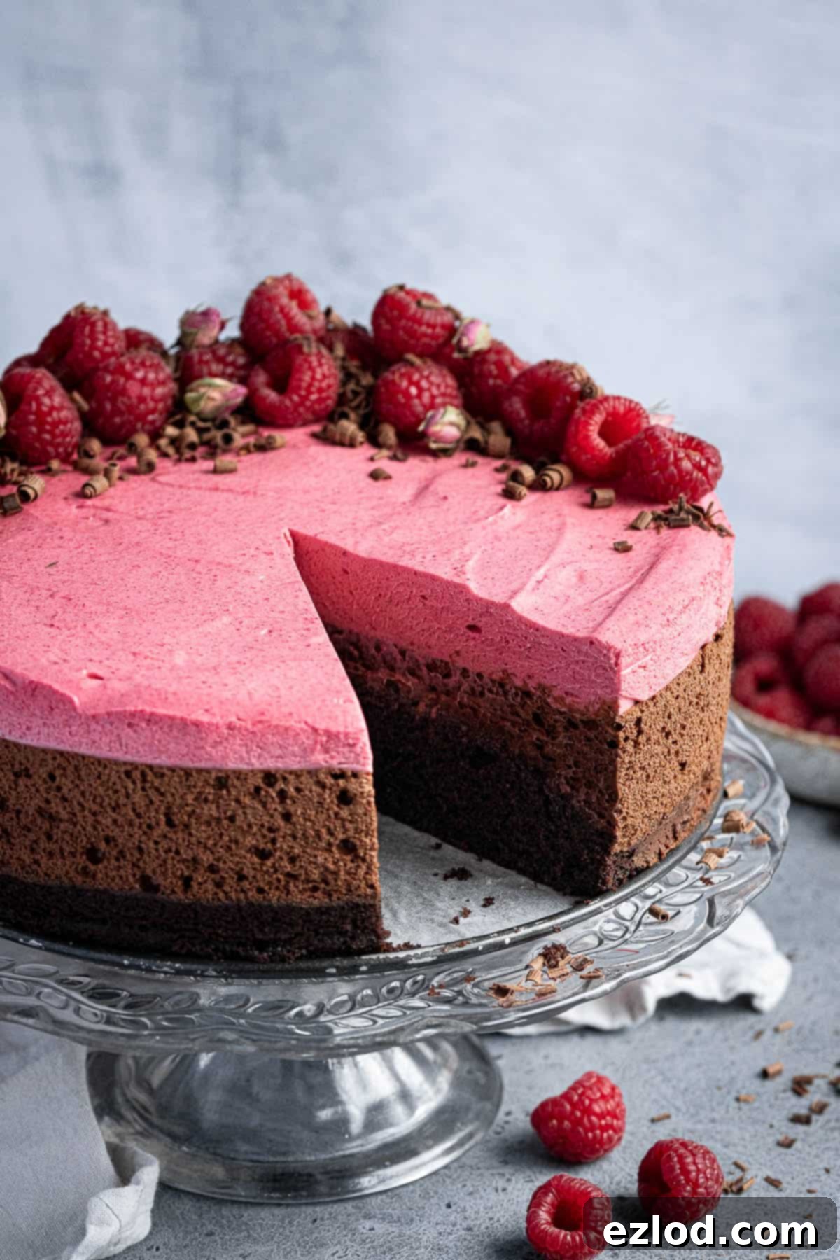 A beautiful close-up of a sliced Vegan Chocolate Raspberry Mousse Cake on a glass cake stand, showing off its perfect layers and inviting texture.