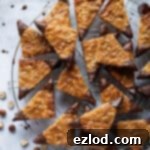Vegan nussecken on a round wire cooling rack with a bowl of chocolate and some scattered hazelnuts.