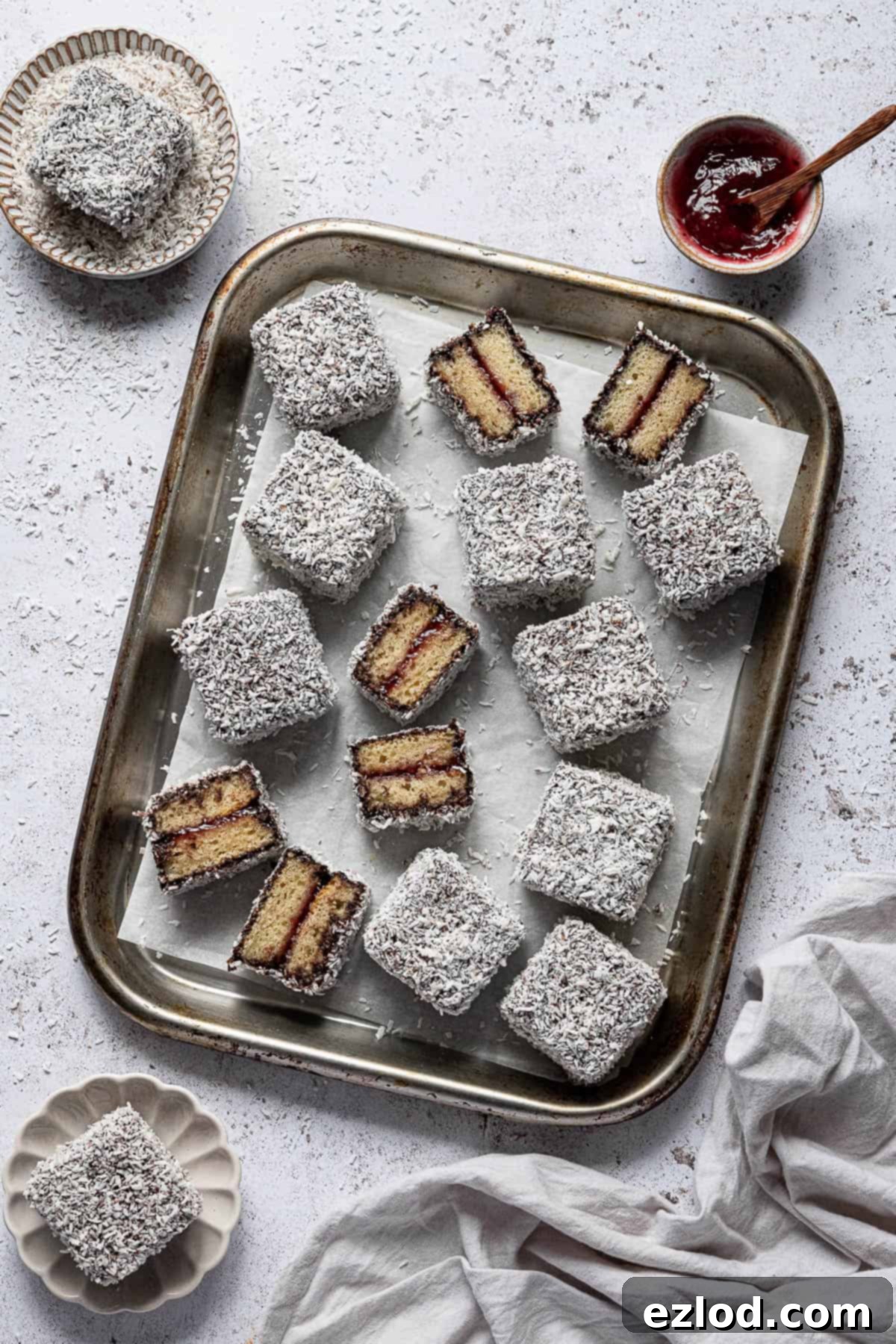 Vegan Lamingtons on a metal baking sheet with bowls of coconut and jam.