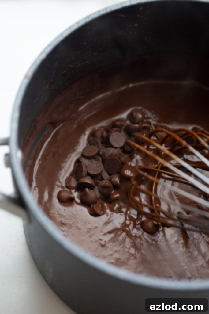 A close-up of dairy-free chocolate chips being whisked into a pot of warm, freshly made vegan chocolate pudding, melting into the creamy mixture.