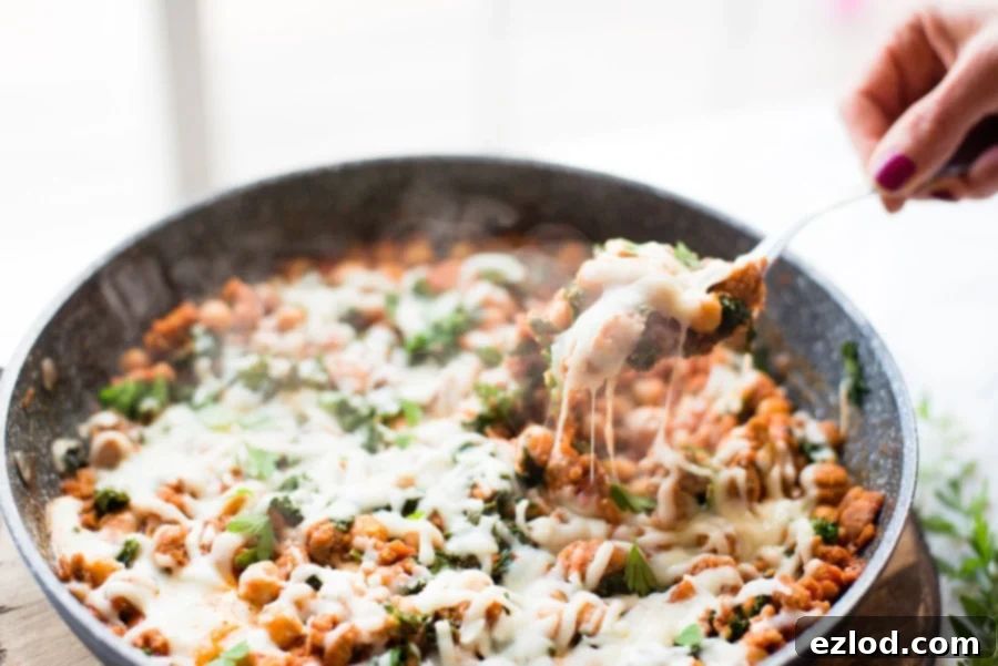 A warm, bubbling Healthy Sausage, Bean, and Kale Skillet fresh off the stove, topped with melted mozzarella cheese and ready to serve.